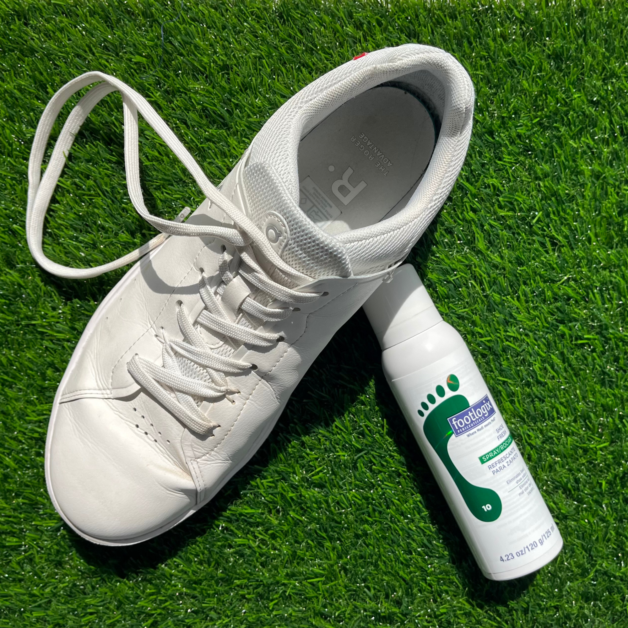 Footlogix Shoe Fresh Spray bottle standing on artificial grass next to a white sneaker with a loose lace.